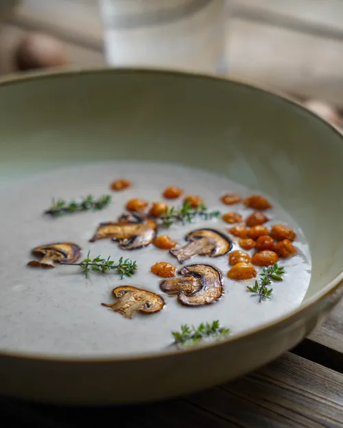 Vegane Champignoncremesuppe in seitlicher Ansicht. Dekoriert mit Thymian und gerösteten Kichererbsen.