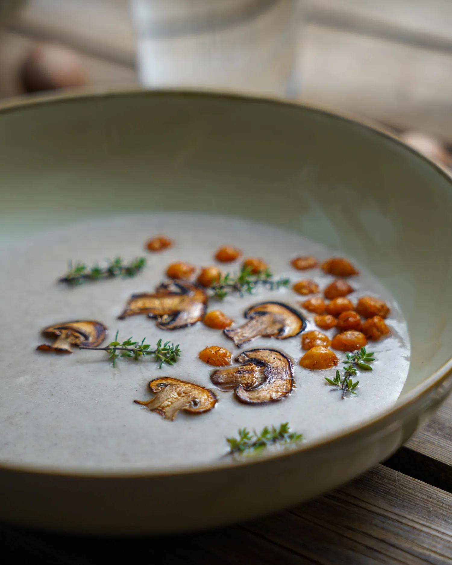 Vegan cream of mushroom soup from the side, garnished with thyme and roasted chickpeas.