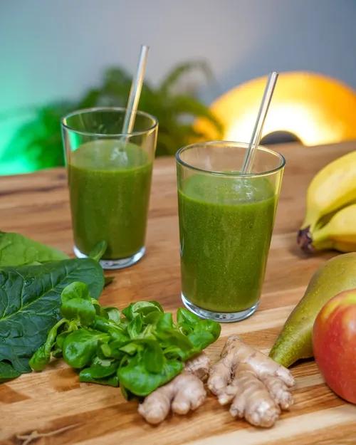 Grüner Smoothie vegan in zwei Gläsern gefüllt. Freundlich dekoriert mit den übrig gebliebenen Zutaten, teaser