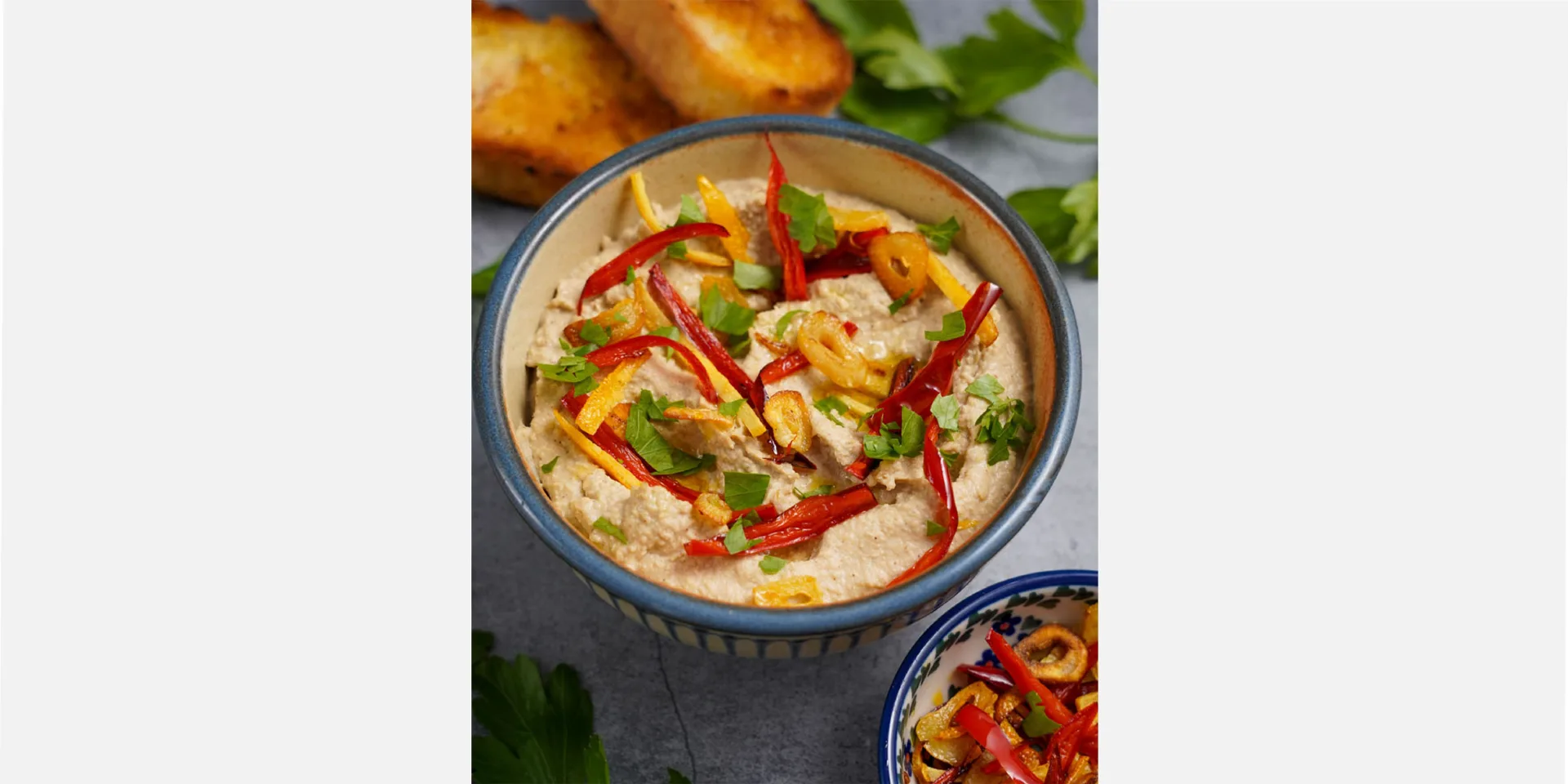 Hummus mit Aromaten vegan in einer Schüssel in der seitlichen Ansicht Hero
