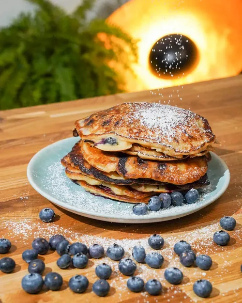 Veganer Pfannkuchen auf dem Teller, dekoriert mit Blaubeeren und Puderzucker, teaser