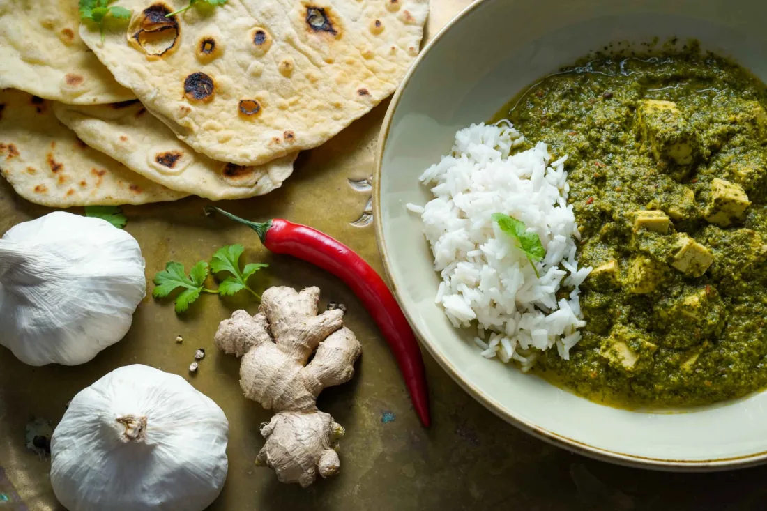 Vegan palak paneer in two bowls with naan bread. Decorated with fresh ingredients like chili and garlic. Close-up.