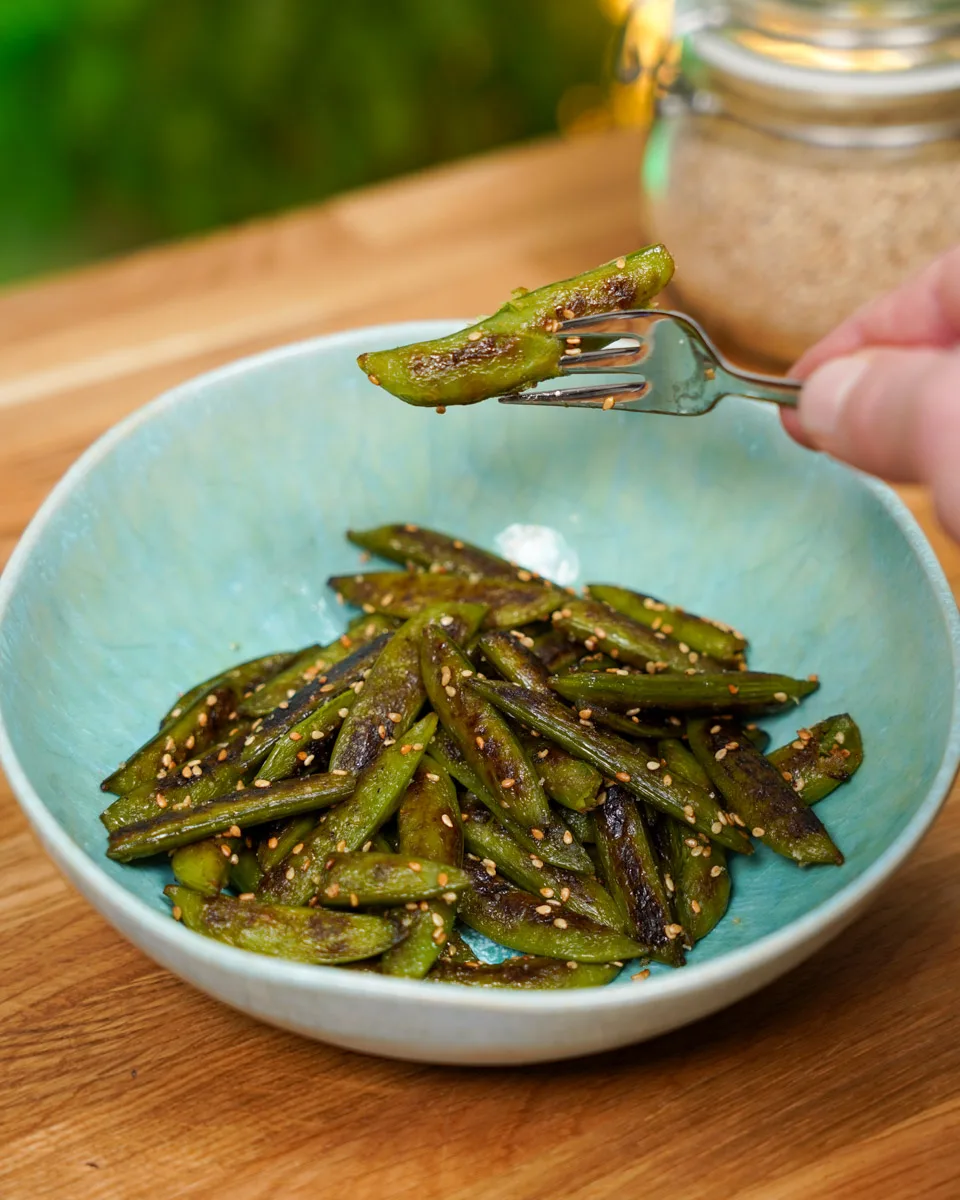 Snow peas served on a plate. One pod picked up with a fork and held up to the camera.