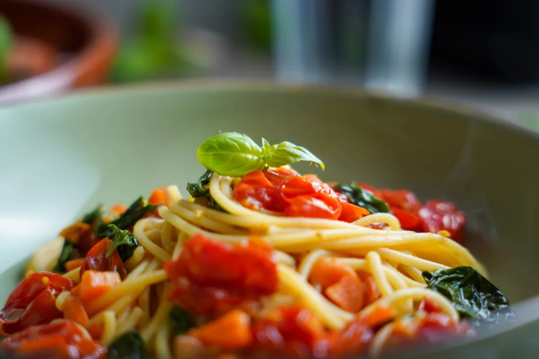 Vegan spaghetti pomodoro served on a plate. Focus on a basil leaf sitting on top of the pasta.