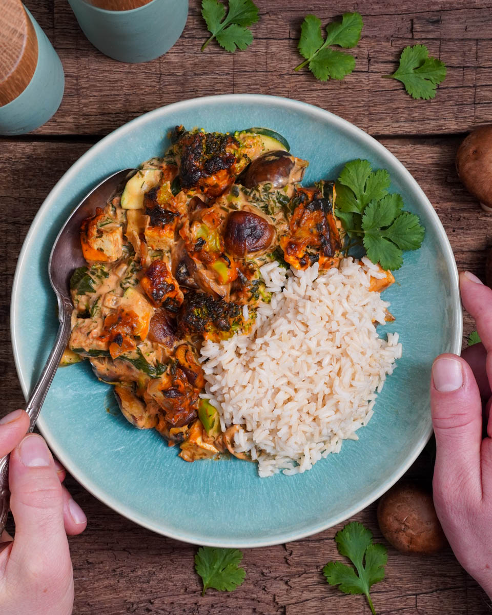 Zwei Hände umfassen einen Teller, welcher den veganen Schlemmertopf und Reis enthält