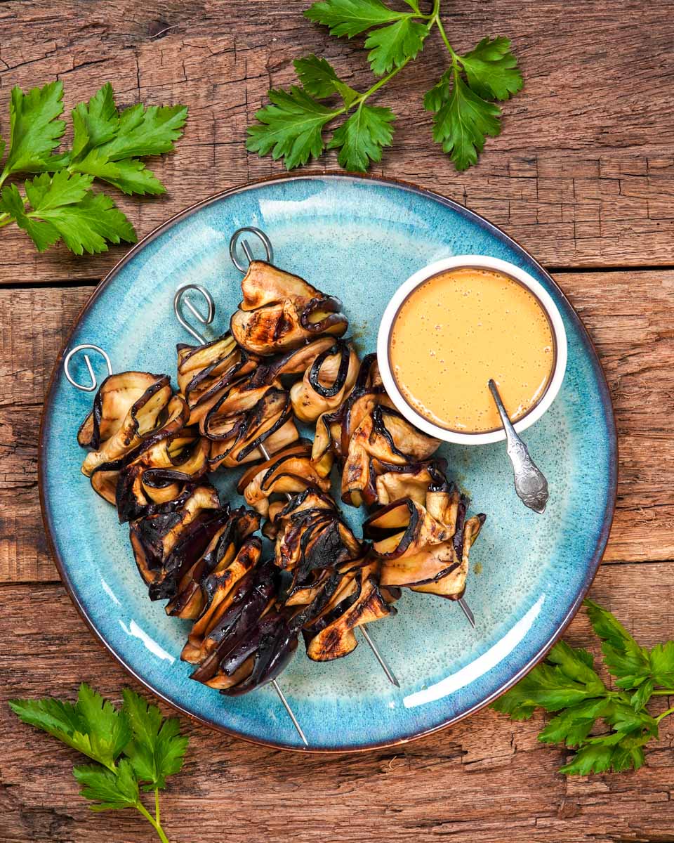 Auberginen-Sate auf einem Teller angerichtet, dekoriert mit veganer Erdnusssauce