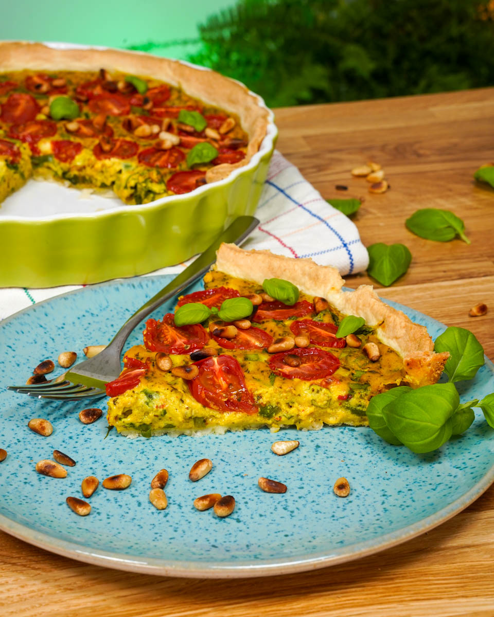 Vegane Quiche auf einem Teller angerichtet, mit Pinienkernen dekoriert
