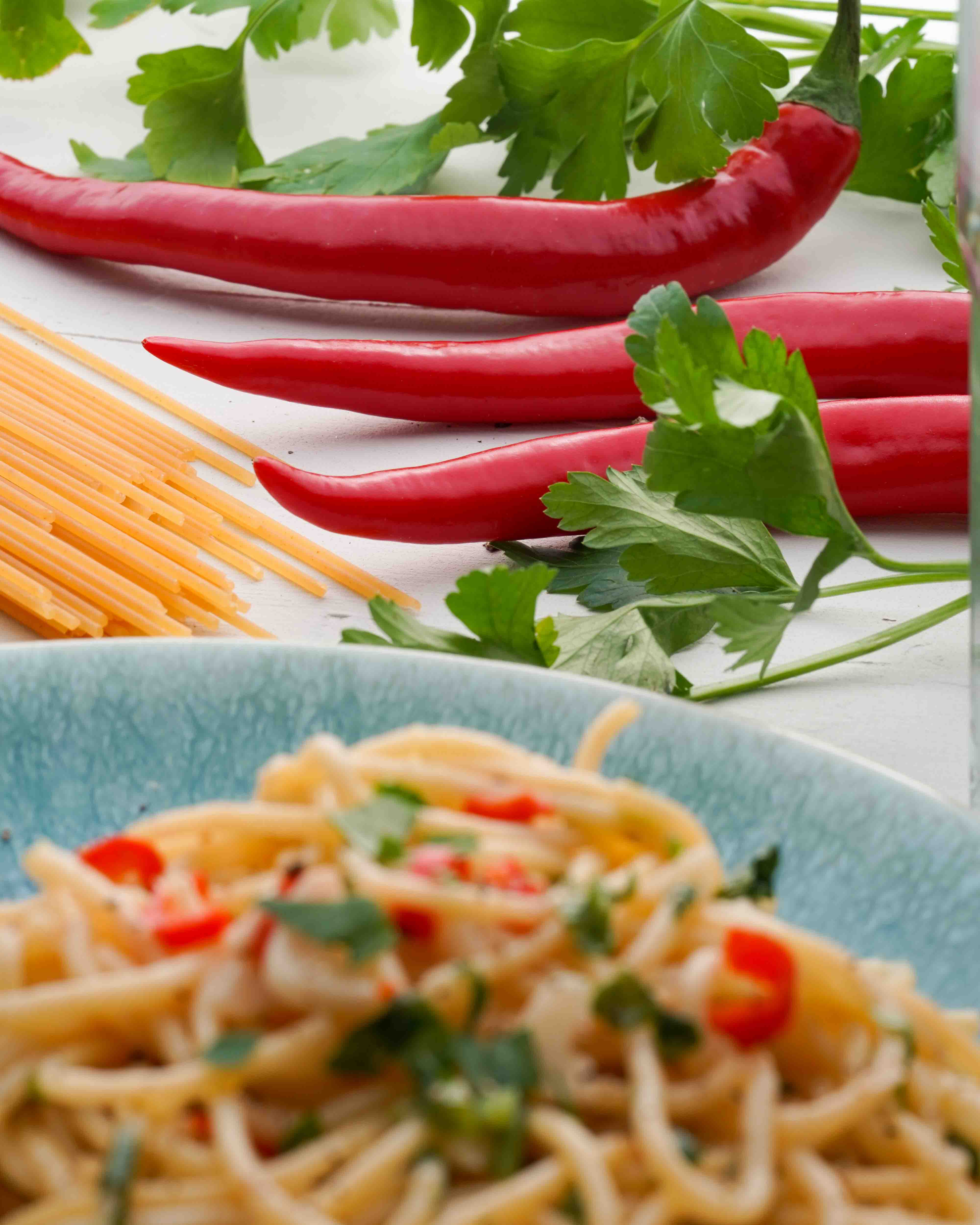 Detailaufnahme von Chili. Im Vordergrund vegane Spaghetti Aglio e olio Detailaufnahme von Chili. Im Vordergrund vegane Spaghetti Aglio e olio