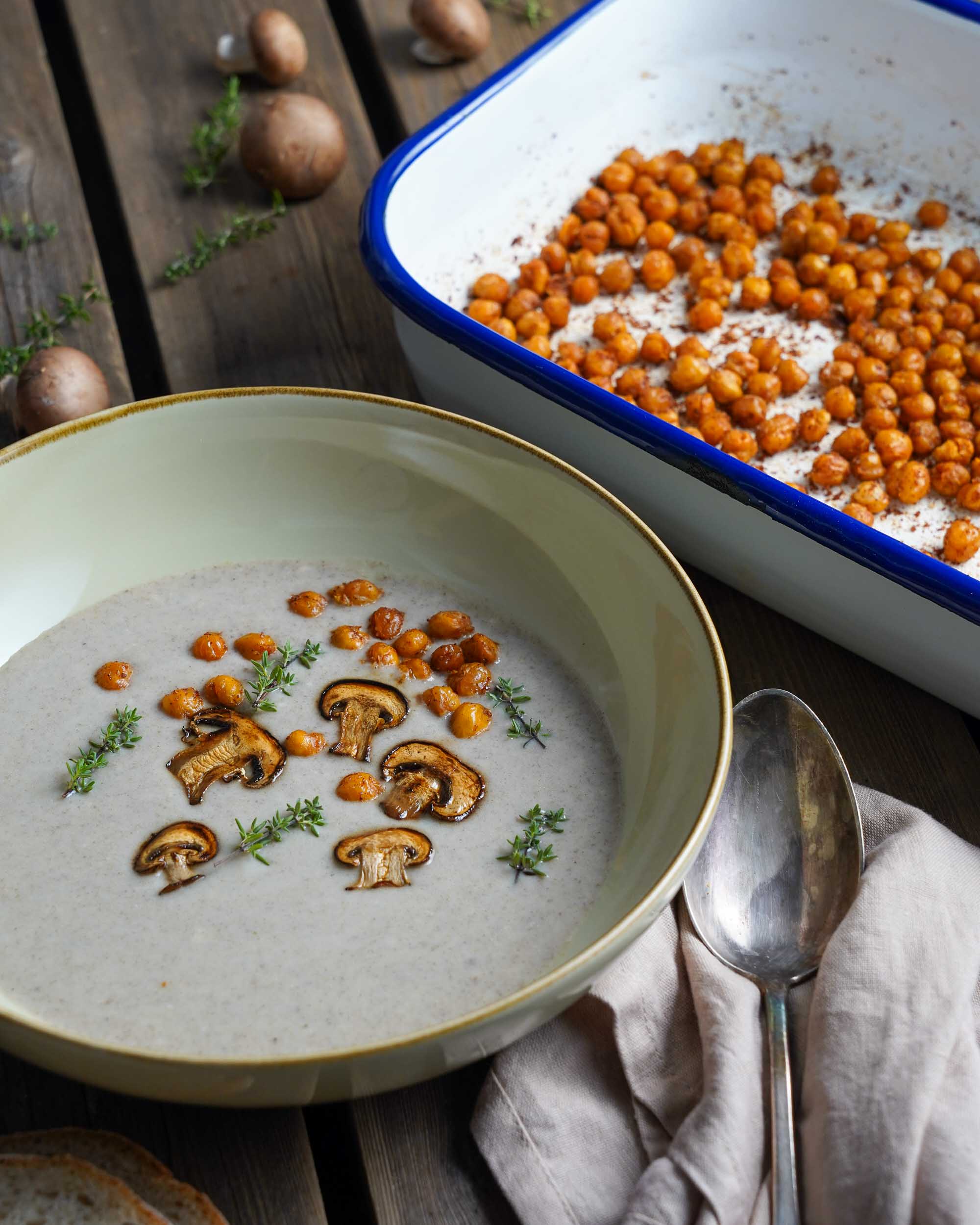 Blick auf die fertige Champignonsuppe mit Pilzen, Thymian und gerösteten Kichererbsen als Toppings. Schön angerichtet auf einem Holztisch. Blick auf die fertige Champignonsuppe mit Pilzen, Thymian und gerösteten Kichererbsen als Toppings. Schön angerichtet auf einem Holztisch.