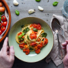Veganes Spaghetti Pomodoro in einem Teller angerichtet. Dekoriert mit vielen frischen Zutaten wie Tomaten, Karotten und Knoblauch. In der Draufsicht.