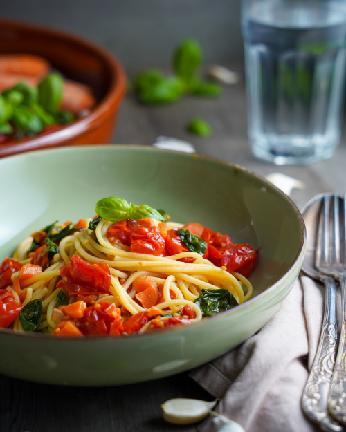 Veganes Spaghetti Pomodoro in einem Teller angerichtet. Dekoriert mit vielen frischen Zutaten wie Tomaten, Karotten und Knoblauch. In der Seitenansicht.