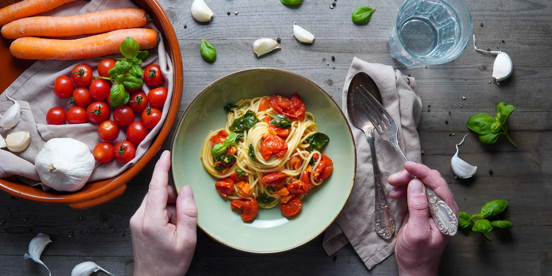 Veganes Spaghetti Pomodoro in einem Teller angerichtet. Dekoriert mit vielen frischen Zutaten wie Tomaten, Karotten und Knoblauch. In der Draufsicht.